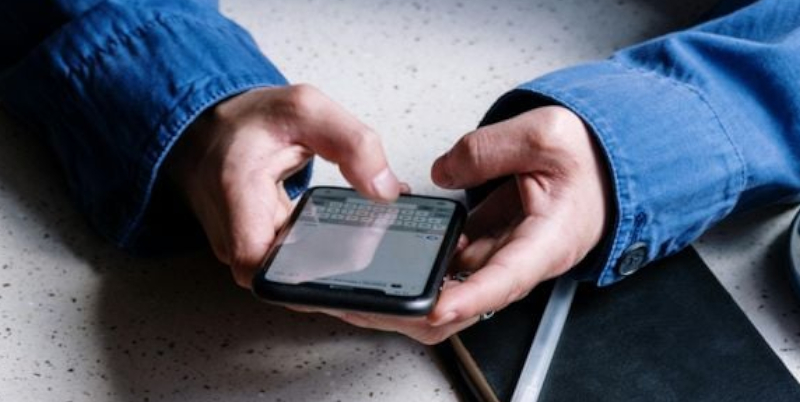 Ein Smartphone wird von einer Person über einen tisch gehalten.